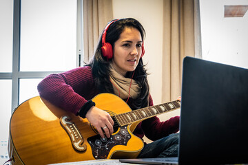 Stock photo of happy woman playing her guitar while following tutorial in her laptop.