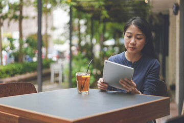 Portrait of a cheerful Asian woman while sitting in a coffee shop with a tablet in her hands