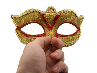 A man holds in his hand a traditional golden carnival Venetian mask with a red ornament on a black background. Preparation for the Brazilian Festival and Mardi Gras, fat Tuesday.