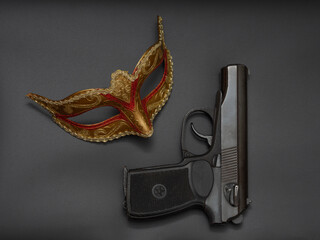 Gun, pistol, traditional golden carnival Venetian mask with red ornament on black background. Preparation for the Brazilian Festival and Mardi Gras, fat Tuesday. The concept of anonymous crime.