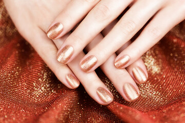 Female hands with bronze-colored manicure on a shiny bronze background. Bronze manicure.