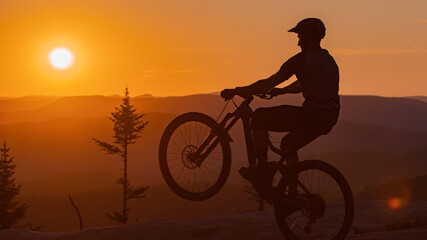 Silhouette of a cyclist doing a wheelie against sunset.  