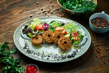 Appetizing salad in the style of oriental cuisine. Fresh vegetable salad with falafel and olive oil served in a blue plate on a wooden background. Restaurant food