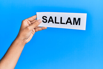 Hand of hispanic man holding sallam word paper over isolated blue background.
