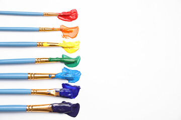 Set of brushes with different paints on white background, flat lay. Rainbow colors