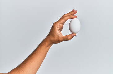 Young hispanic hand holding raw egg over isolated white background.