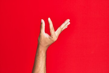 Arm of caucasian white young man over red isolated background picking and taking invisible thing, holding object with fingers showing space