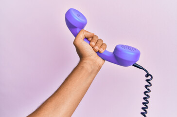 Hispanic hand holding vintage telephone over isolated pink background.