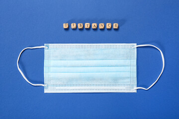 Medical face mask and word Distance made with small wooden cubes on blue background, flat lay