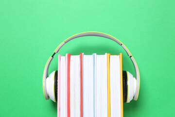 Books with modern headphones on green background, top view