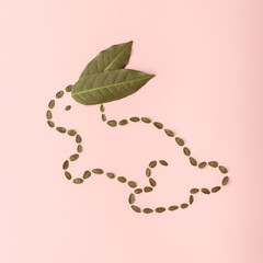A rabbit shape made of green leaves on a pink background. Easter  creative arrangement   concept. Flat lay frame. Minimal style.