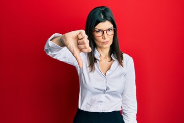 Young hispanic woman wearing business shirt and glasses looking unhappy and angry showing rejection and negative with thumbs down gesture. bad expression.