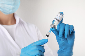 Doctor filling syringe with vaccine against Covid-19 on white background, closeup