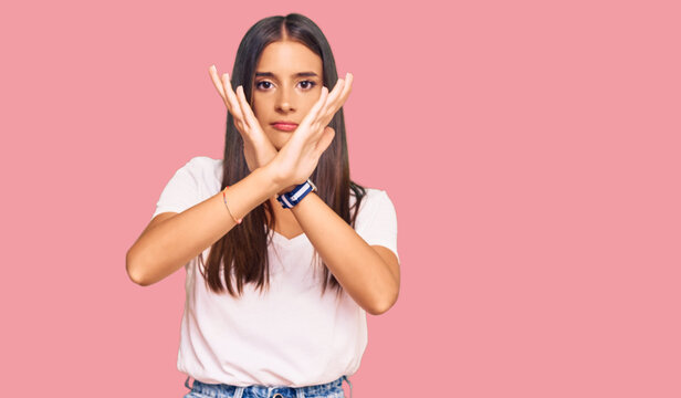 Young hispanic woman wearing casual white tshirt rejection expression crossing arms doing negative sign, angry face