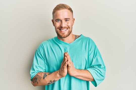 Young caucasian man wearing casual clothes praying with hands together asking for forgiveness smiling confident.