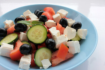 Greek salad in blue bowl on white background. Close-up of vegetable salad with fets cheese, black olives, cucumber and tomatoes. Top view, copy space
