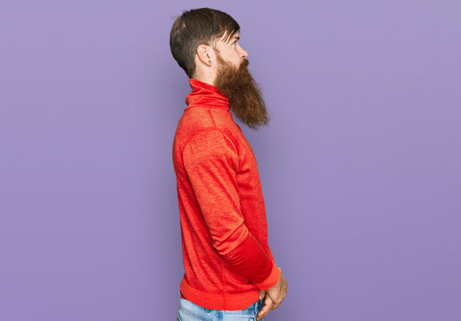 Redhead man with long beard wearing casual clothes looking to side, relax profile pose with natural face with confident smile.