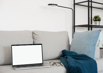 Blank screen laptop computer mockup over white modern living room design. View of modern scandinavian style interior with sofa. Home staging and minimalism concept