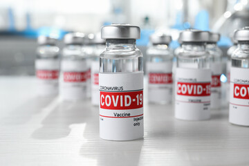 Glass vials with COVID-19 vaccine on white wooden table