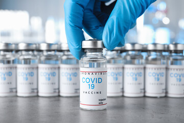 Doctor taking glass vial with COVID-19 vaccine from table, closeup