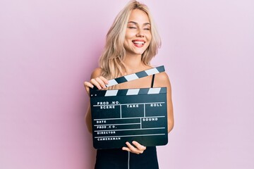 Beautiful caucasian blonde girl holding video film clapboard smiling and laughing hard out loud...