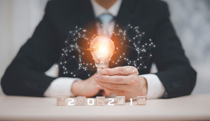 Businessman hand holding light bulb with icon on wood cube and   working on desk, Creativity and innovation are keys to success.Concept of new idea and innovation with Brain and light bulbs, working a