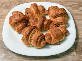 A few croissants on the large white plate over the wooden table. Close-up. Still life.