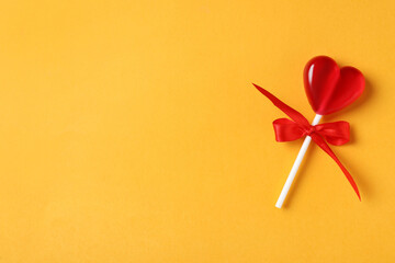 Sweet heart shaped lollipop on orange background, top view with space for text. Valentine's day...