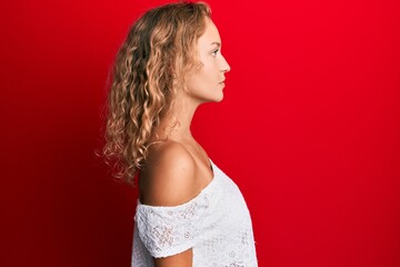 Obraz premium Beautiful caucasian woman wearing casual clothes over red background looking to side, relax profile pose with natural face with confident smile.
