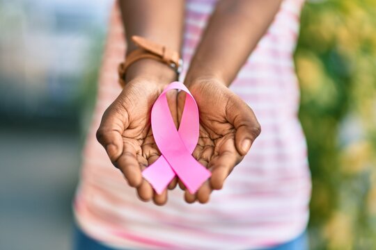 Hands of african american girl holding pink breast cancer ribbon at the park.