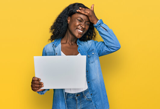 Beautiful african young woman holding blank empty banner stressed and frustrated with hand on head, surprised and angry face