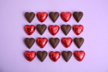 Tasty heart shaped chocolate candies on violet background, flat lay. Happy Valentine's day