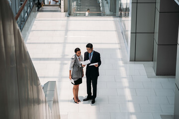 Two business people reading business papers documents.
High view of serious businessman and businesswoman standing in office hall and reading upset news