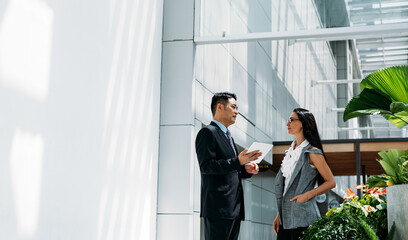 Businessman holding tablet and talking with businesswoman inside modern office building.
Happy business team of two colleagues working on digital tablet together in modern office interior