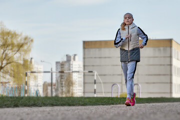 Fototapeta premium Portrait of a beautiful athletic girl running on a treadmill on a blurry school background