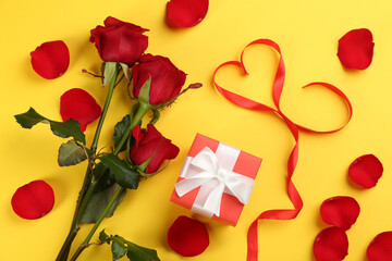 Flat lay composition with beautiful red roses and gift box on yellow background. Valentine's Day celebration