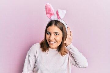 Young beautiful woman wearing cute easter bunny ears smiling with hand over ear listening an hearing to rumor or gossip. deafness concept.