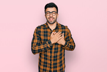 Hispanic man with beard wearing casual clothes and glasses smiling with hands on chest with closed eyes and grateful gesture on face. health concept.