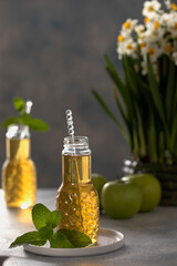 Close up of fresh apple juice in bottles on table with green apples mint and bouquet of daffodils. Fresh healthy drink. High quality photo