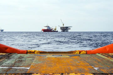 An anchor handling tug boat leaving an offshore oil production platform with a construction vessel moored next to it