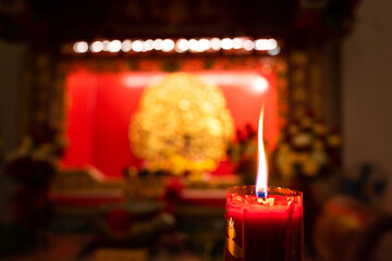 Close-up at candlelight during in burning with blurred background of the Chinese shrine. Selective focus the at the candle's core.