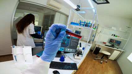 Naklejka premium FPV of scientist holding blood sample from test tube analysing and typing on pc vaccine evolution. Team of doctors, viorolog researcher in professional lab working to discover medical treatment.