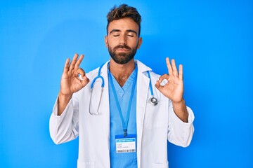 Young hispanic man wearing doctor uniform and stethoscope relax and smiling with eyes closed doing meditation gesture with fingers. yoga concept.