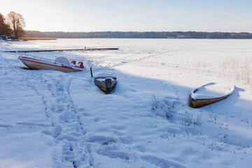 Old boats on the shore of a frozen lake. Footprints in the snow