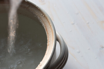 water flowing into clay pot on white wood background from above