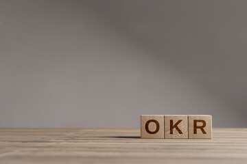 Wood cubes with acronym 'OKR' - 'Objectives and Key Results' on a beautiful wooden table, studio...