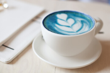 Unfocused woman hands holding cup of hot butterfly pea latte or blue spirulina latte on wooden table