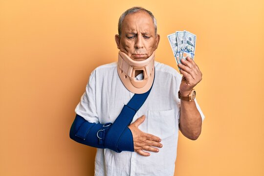 Handsome mature injured man wearing cervical collar and sling holding insurance money depressed and worry for distress, crying angry and afraid. sad expression.