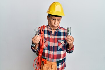 Senior hispanic man wearing handyman uniform holding led lightbulb and incandescent bulb skeptic and nervous, frowning upset because of problem. negative person.