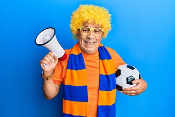 Senior hispanic man football hooligan cheering game holding ball and megaphone smiling and laughing...
